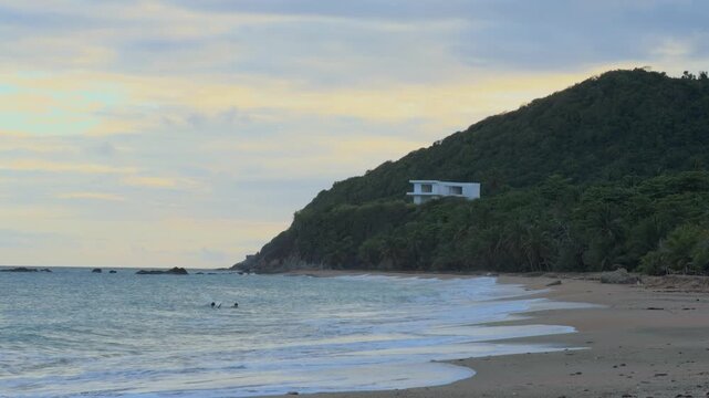 view of gentle ocean waves rolling onto a tropical sandy beach with a lush green mountain hill in Puerto Rico