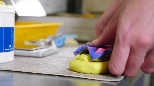 Dental technician working with metal instrument onto yellow and blue jaw impression mold. Creating precise artificial master model for manufacturing custom dental crowns and prosthetic restoration. 4k