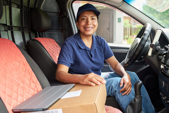 Portrait of Hispanic female courier smiling in delivery van with cardboard box. Image represents logistics and shipping services, suitable for e-commerce marketing