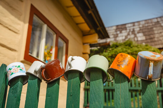 Collection of vintage enamel mugs displayed on a rustic wooden fence outdoors