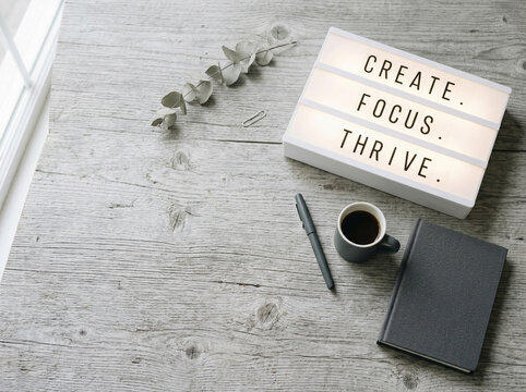 Light box with motivational text on a wooden desk with coffee and notebook