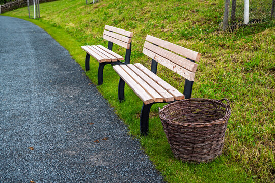 Two wooden park benches sit beside a gravel path with a woven basket