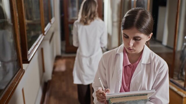 Young adult Caucasian female medical student in lab coat examining anatomical specimens and writing notes in anatomy museum. Clip is perfect for medical school advertising