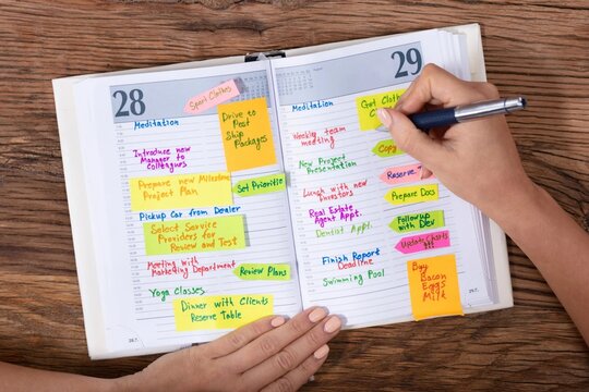 Person writing in an open daily planner with colorful markers and sticky notes calendar schedule organizer