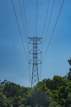 Symmetrical low angle view of a tall high voltage electrical transmission pylon tower with power lines stretching against a clear blue sky.