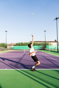 Young man serving tennis ball on court