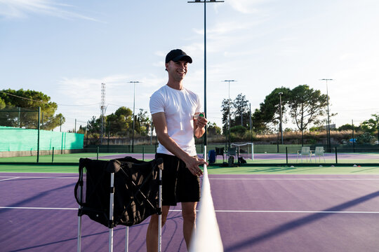 Smiling tennis coach holding ball on court
