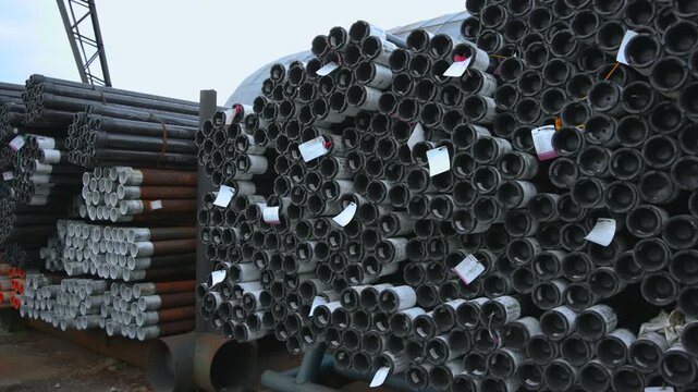 Outdoor industrial yard stacked steel pipes on racks with labeled bundles under overcast sky, low eye-level viewpoint emphasizing repeating circular patterns and inventory depth