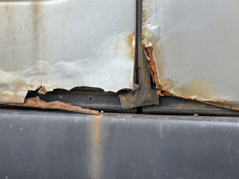 Severe rust and corrosion damage on gray metal car body panels