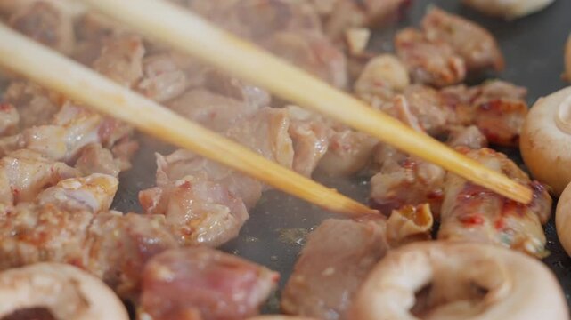 Close-up of stir-fried mutton cubes and white mushrooms on iron plate with chopsticks