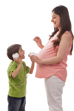 Boy using cups on pregnant mothers belly to listen for baby