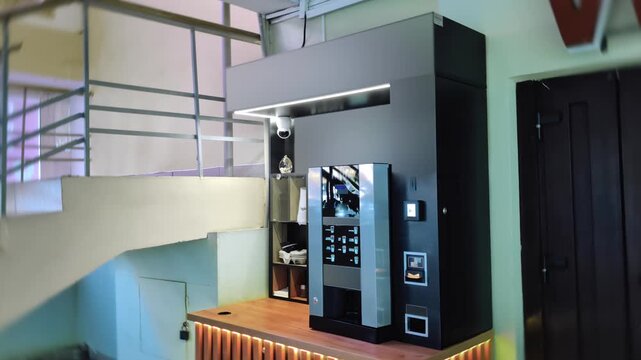Modern self-serve coffee bar setup inside contemporary building. Automated vending machine device with various hot beverages for quick service convenience to employees and visitors.