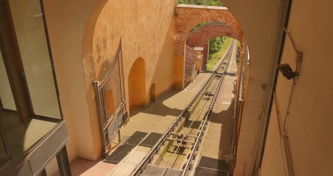 Historic funicular railway tracks leading through an old stone archway and brick gateway during a bright day in Mondovi, Piedmont, Italy.
