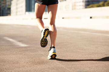Obraz premium Fitness, active and legs in city with running, cardio and stamina exercise in physical activity. Training, space and female person outdoor with jog, sports hobby and athletic workout in town.