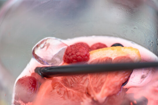 Close-up of a refreshing pink gin cocktail with fresh raspberries and citrus slices