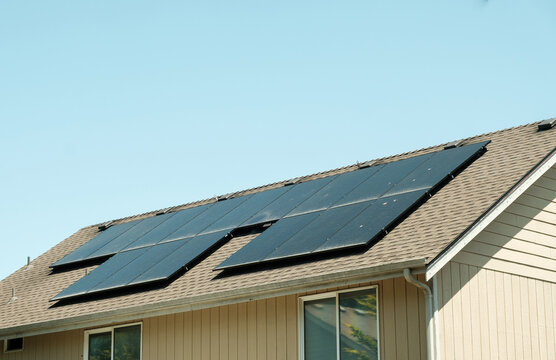 Modern solar panels installed on the shingled roof of a suburban house.