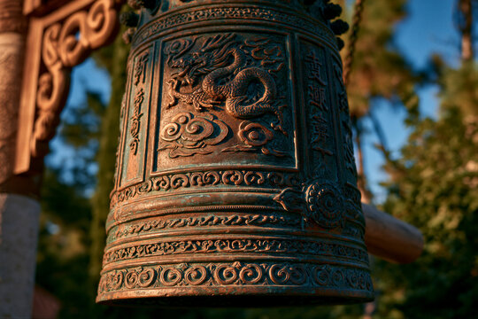 Grand bronze peace bell with traditional dragon motifs on wooden frame, bathed in warm golden light against lush greenery, featuring open copy space for cultural posters and peace campaign banners.