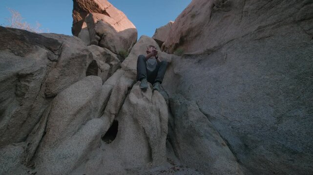 A hiker rests on a rock ledge tucked inside a boulder formation at dusk.