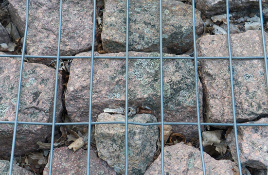 Granite cobblestone pavement texture viewed behind a metal wire mesh grid