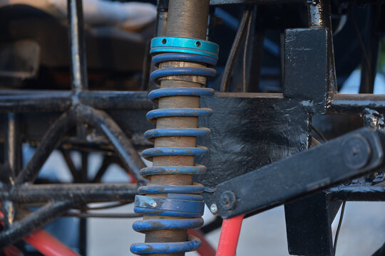 Close up shot of a blue coilover suspension spring mounted on a custom race car frame. Mechanical detail of off road vehicle suspension system, steel frame, and shock absorber parts.