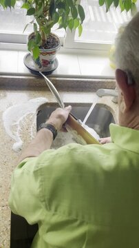 Abuelo lavando y aclarando sart&eacute;n en lavadero pileta de cocina con agua del grifo y jab&oacute;n en encimera de cocina y pila
