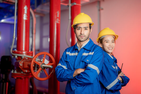 A female and a male engineer standing beside the fire pump valve controls in a fire pump room with red piping and valves. Strong visual for maintenance and quality.