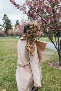 Back view of woman with long wavy hair walking near blooming cherry trees in park.