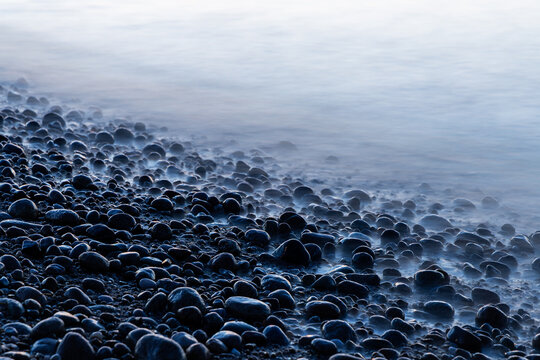 Calm misty water washes over a rocky shore