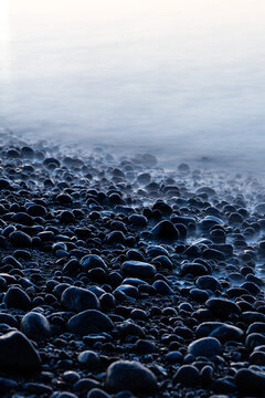 Misty water washes over smooth dark pebbles