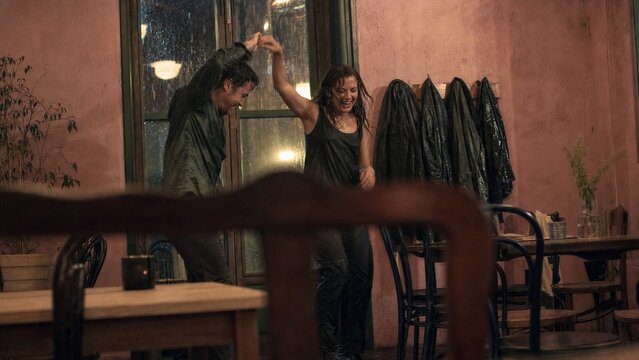 Man and woman dancing in cafe during rain. Happy couple spinning together indoors after getting wet in stormy weather. Impromptu romantic moment, lifestyle concept of joy and love.