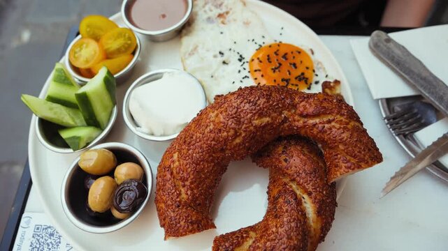 Traditional Turkish breakfast served with crispy simit, fried egg, fresh vegetables, olives and cheese. Authentic morning meal with classic local dishes on a restaurant table. High quality 4k footage