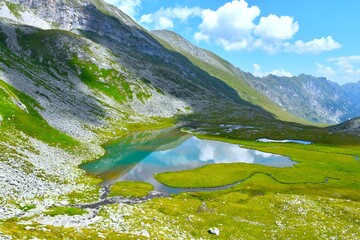 View of Unterer Lanischsee lake with a reflection at the surface bellow rock and green gras covered mountains slopes in Pöllatal valley in High Tauern, Carinthia, Austria © kato08