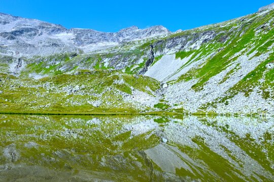View of the mountain peak above the rock cliffs and green meadows above the Unterer Lanischsee high mountain lake 