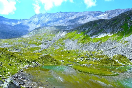 Oberer Lanischsee alpine lake with a small island and a reflection in the water bellow rock and green meadow covered mountain range in P&ouml;llatal, High Tauern, Carinthia, Austria