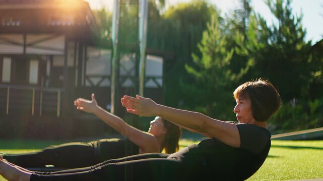 Elderly women practicing slow motion Pilates on yoga mats outdoors, stretching and strengthening core muscles together in a peaceful green garden setting