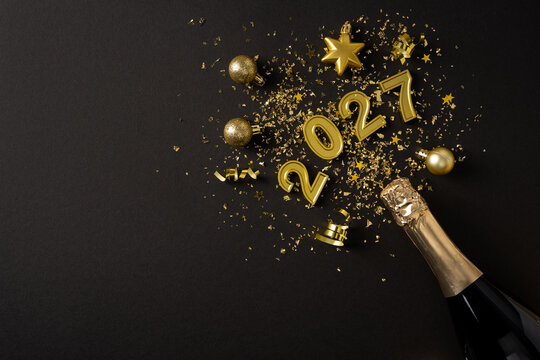 Happy New Year 2027 celebration with gold confetti, champagne bottle and ornaments on black background