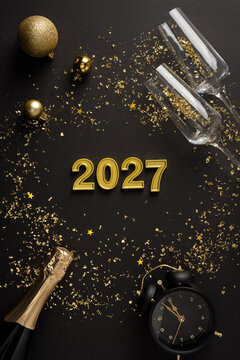 Happy New Year 2027 celebration with champagne, confetti, clock and golden decoration on vertical black backdrop