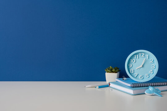 Side view photo of blue desk with clock, notebooks and pen for back to school study
