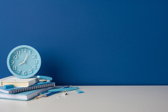 Side view photo of back to school desk with blue clock and stationery