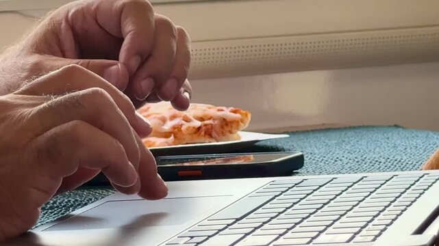 Hands on laptop trackpad and keyboard with smartphone and snack on desk &mdash; home office