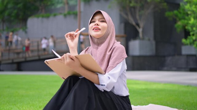Asian young Muslim woman taking notes in her diary journal in the city.
