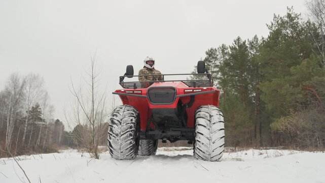 Red atv tearing through snowy trail, solo helmeted rider powering through packed snow, deep tread tires kicking flurries, pine forest edge, low frontal angle, overcast sky, gritty highenergy mood,