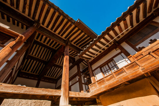 Traditional Korean hanok vernacular architecture vertical low-angle perspective featuring wooden pillars, rafters, and tiled roofs against blue sky