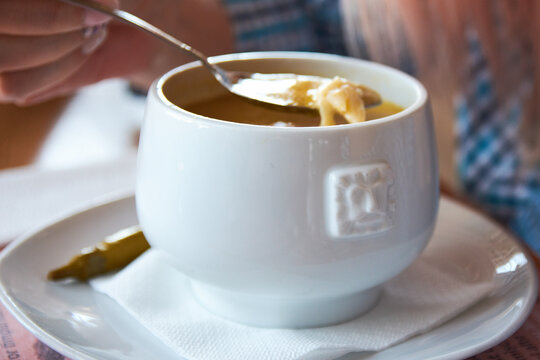 Close-up of a person eating traditional romanian tripe soup from a white bowl.