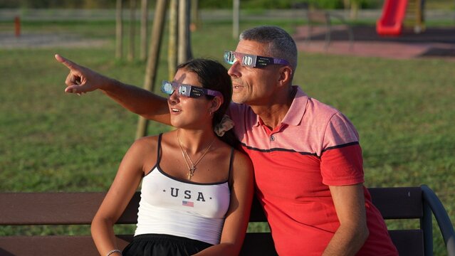 Man and daughter observing total solar eclipse with special protective glasses outdoors