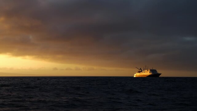 A cruise ship in The Gal&aacute;pagos Islands reflects the color of the setting sun (4K).