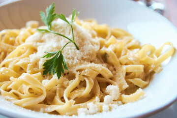 Close-up of freshly cooked fettuccine pasta topped with grated parmesan cheese and fresh parsley in a white bowl © Radu Bighian