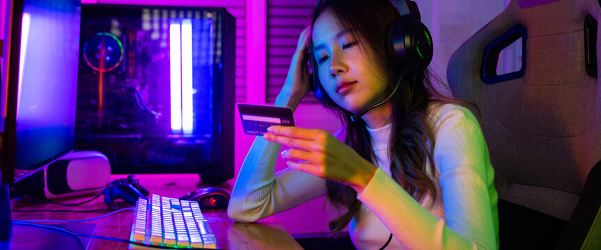 Young Asian woman gamer wearing headphones unset suffer of overspending money from card account after pay game online, problem using credit card