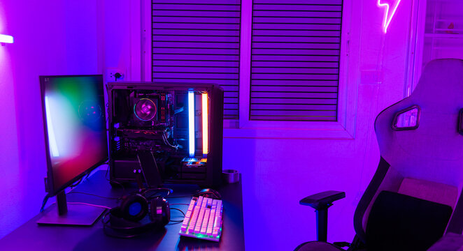 A computer setup with a purple light dark background, games transmission modern equipment, modern gaming PC on desk with keyboard mouse monitor