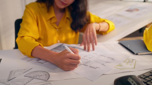 Young Hispanic woman architect sitting at desk, working in an office.